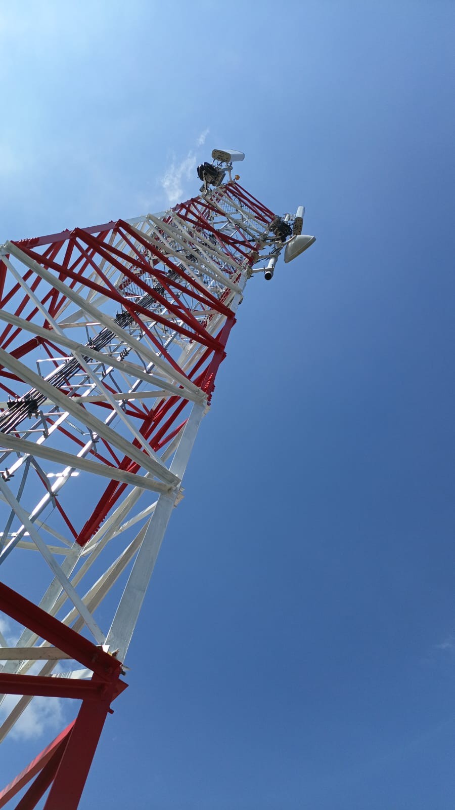 Red and white lattice tower with antennas against a blue sky