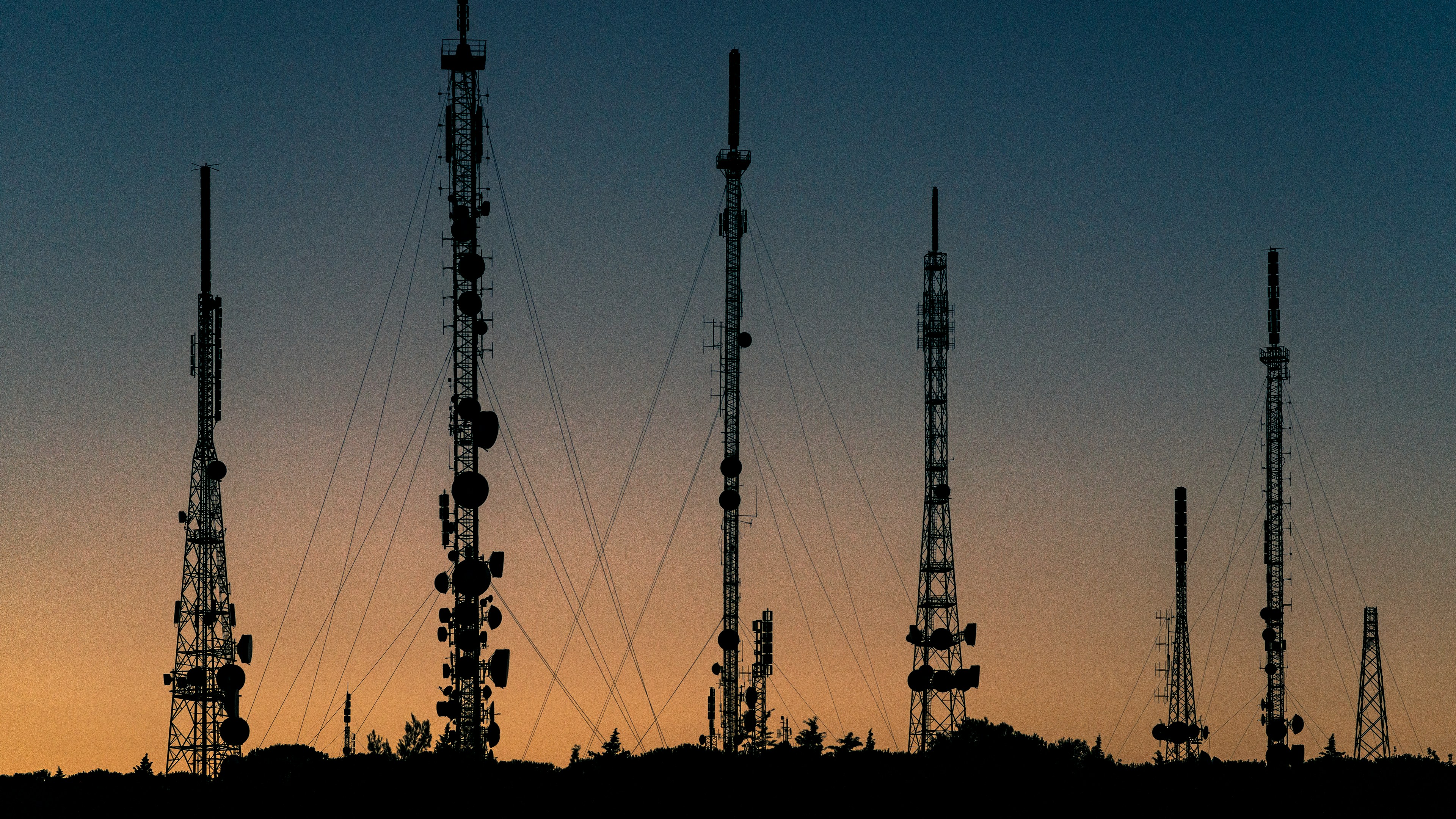 Telecom towers silhouetted against a sunset sky